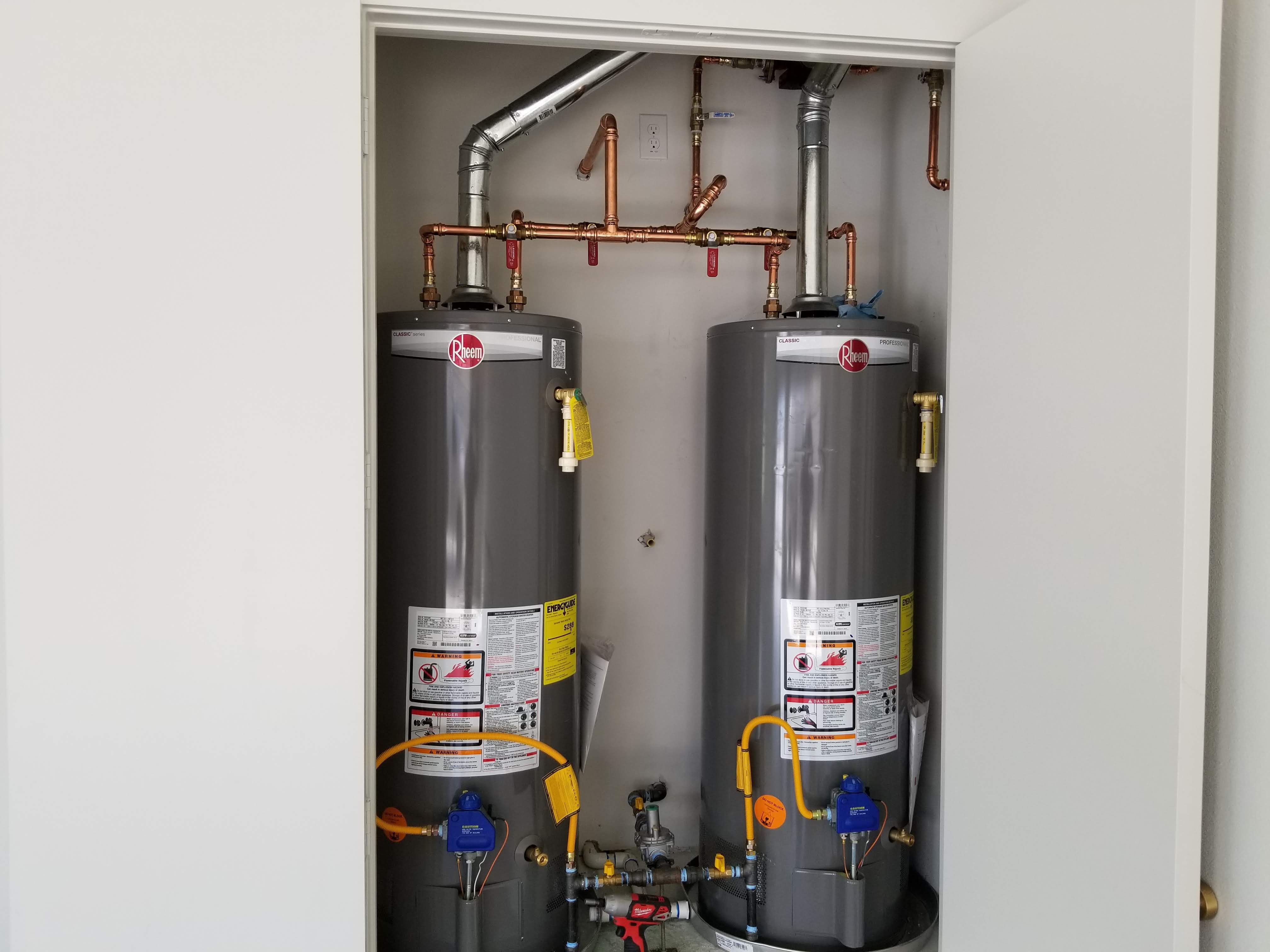 Two new gas tank water heaters installed side by side in a closet