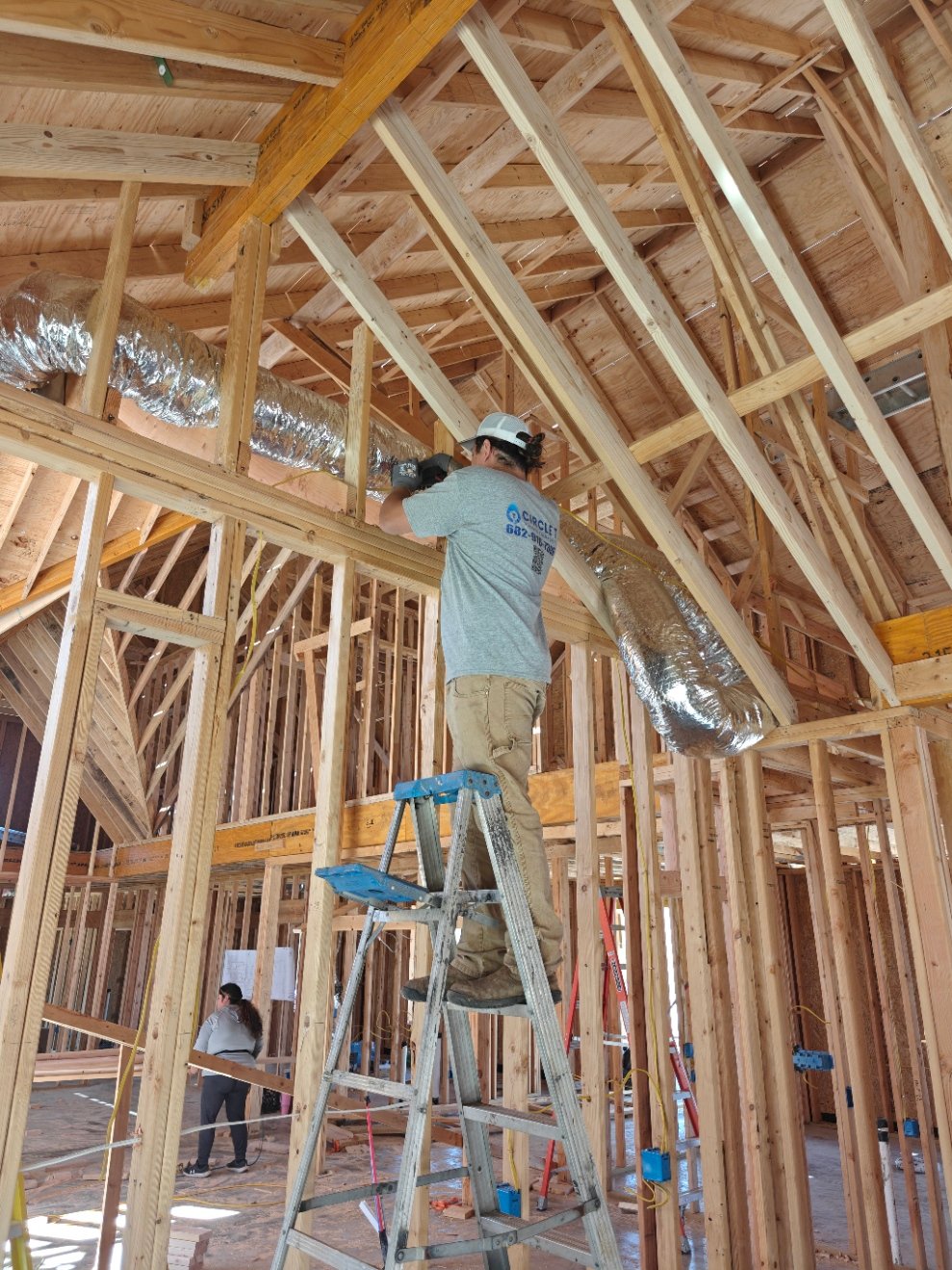Plumber on a ladder running top-out plumbing in a framed new home
